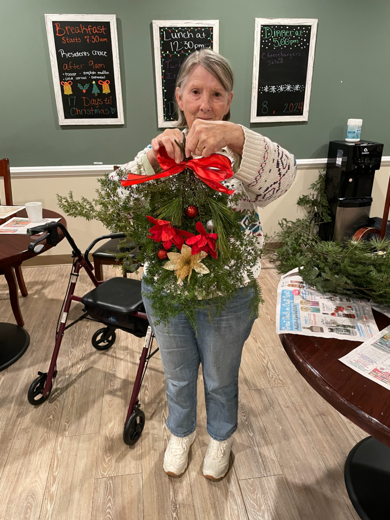 A resident is standing, holding up a wreath they made.