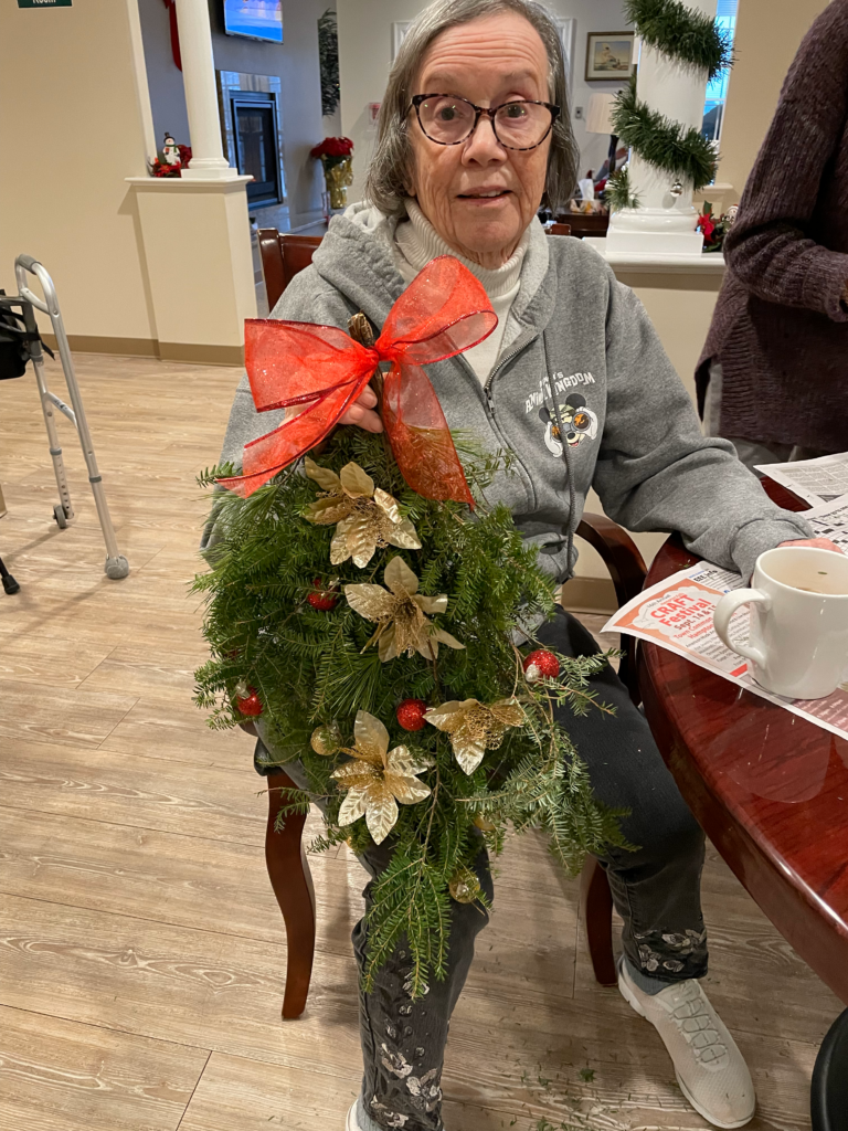 A resident is seated, holding a wreath they made.